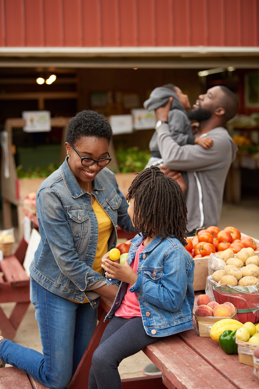 A mother introduces fresh plums to her daughter at a farm stand.