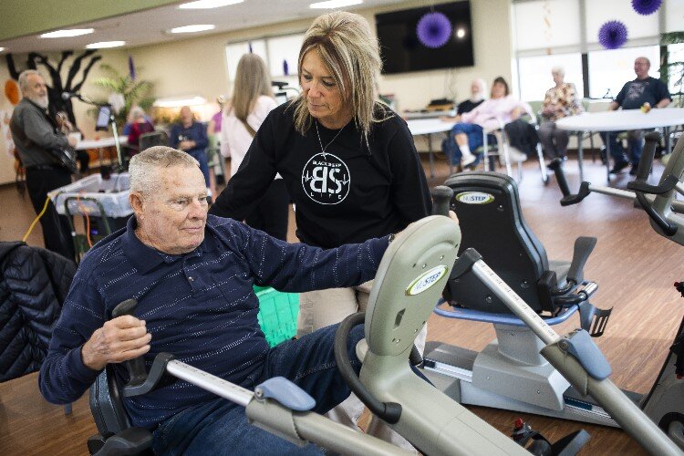 Julie Dilts assists Jim Harner, a resident, while he uses an exercise bike.