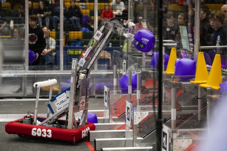 A robot grabs hold of an object while teams compete in the FIRST.