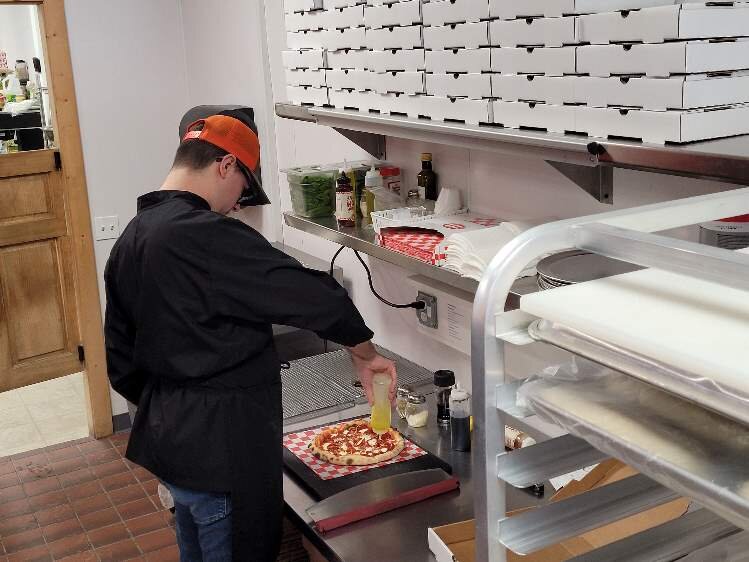 Jameson Baker puts the final touches on a pizza.