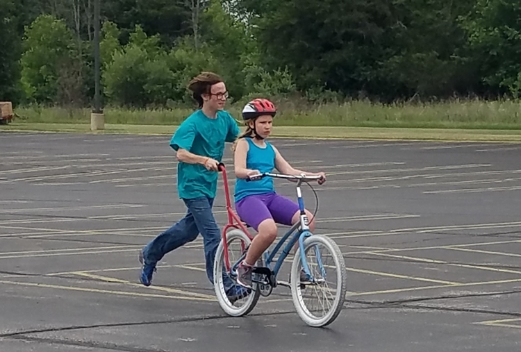 A girl learns to ride with the help of a volunteer and the I Can Bike Midland program.