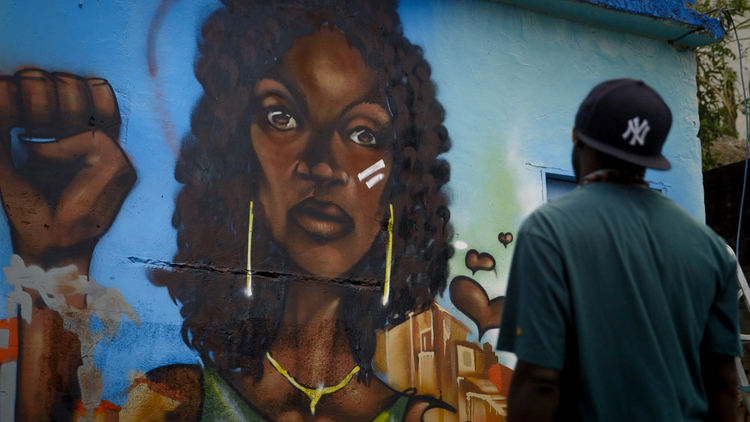 On the first day of the 2014 FIFA World Cup, Brazilian Graffiti artist Panmela Castro organizes a 1 kilometer-long mural protesting domestic violence in Little Stones.