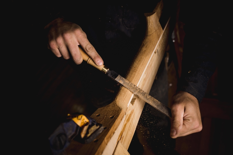 Matt Eich carves the neck of a guitar in process.