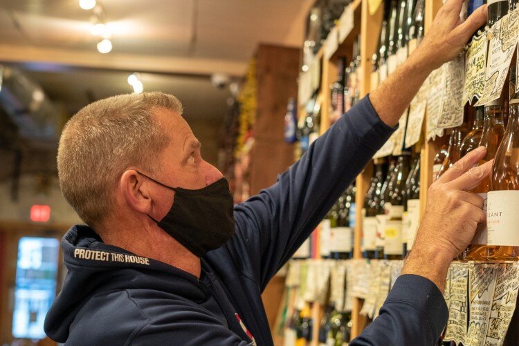 Greg Kimbrue wears a mask while posting notes that explain what to expect from the wines on his shelves.