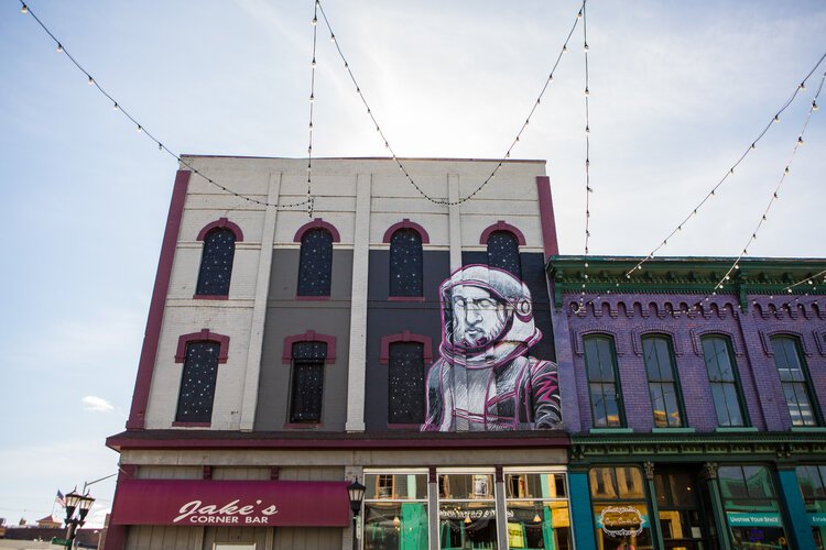 Looking up from Third Street, a massive astronaut is illuminated by the Third Street Star Bridge, floating above the “stars” in outer space.