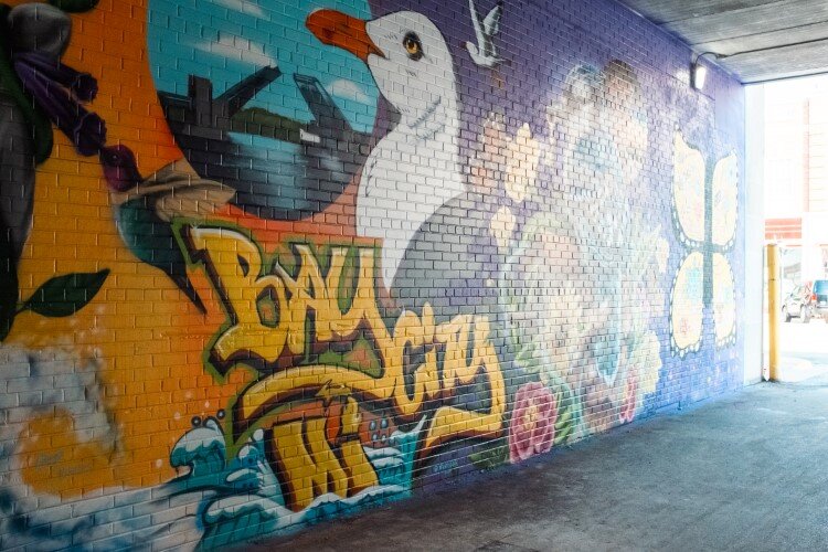 The murals line one wall of the alley, merging from one scene into another.