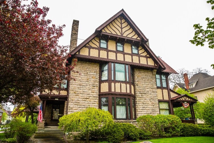 Features include the home’s stucco and half-timbering inserts. It has multiple intersecting gables, giving it Tudor Revival elements.