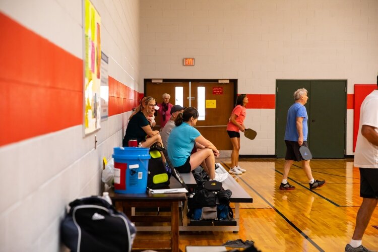 Players constantly change partners at the Bay County Community Center. A rule board on the wall explains how players rotate in and out of play, specifying that no one plays more than two games in a row. In between rounds, players wait on a bench.